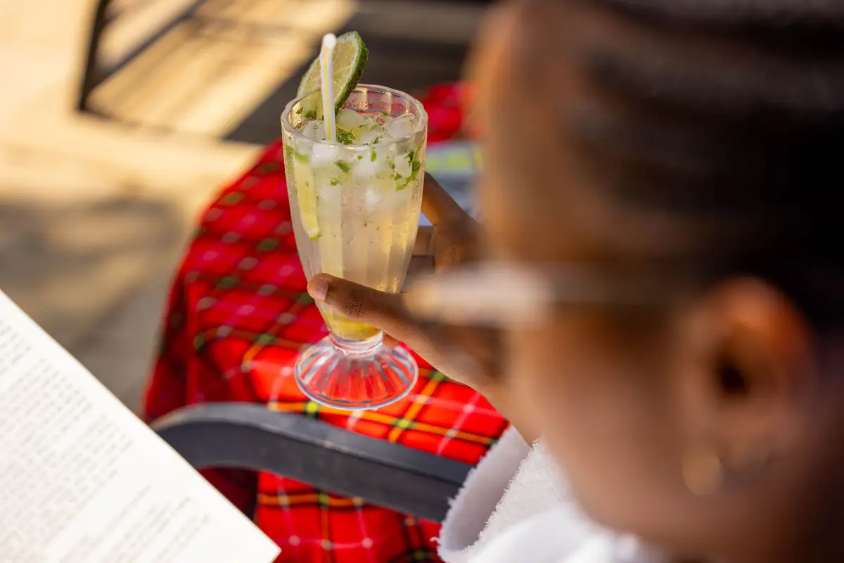 Guest reading with a drink by the pool at Mvuli Farm Lodge